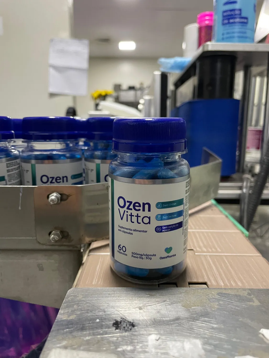 Frasco de OzenVitta próximo a uma linha de produção